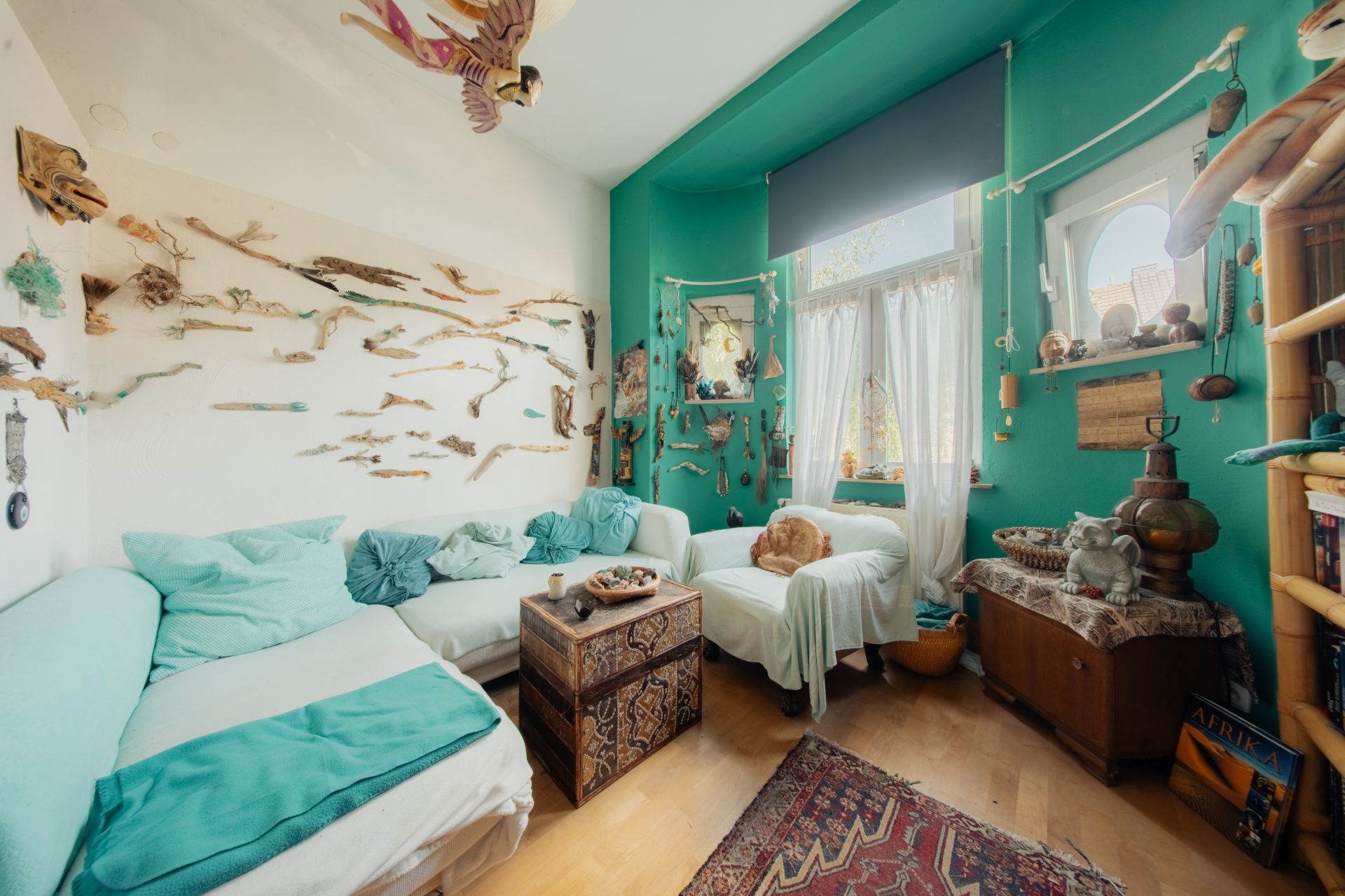 Wohnzimmer mit türkisfarbenen Wänden, weißen Sofas und vielen dekorativen Gegenständen an den Wänden.