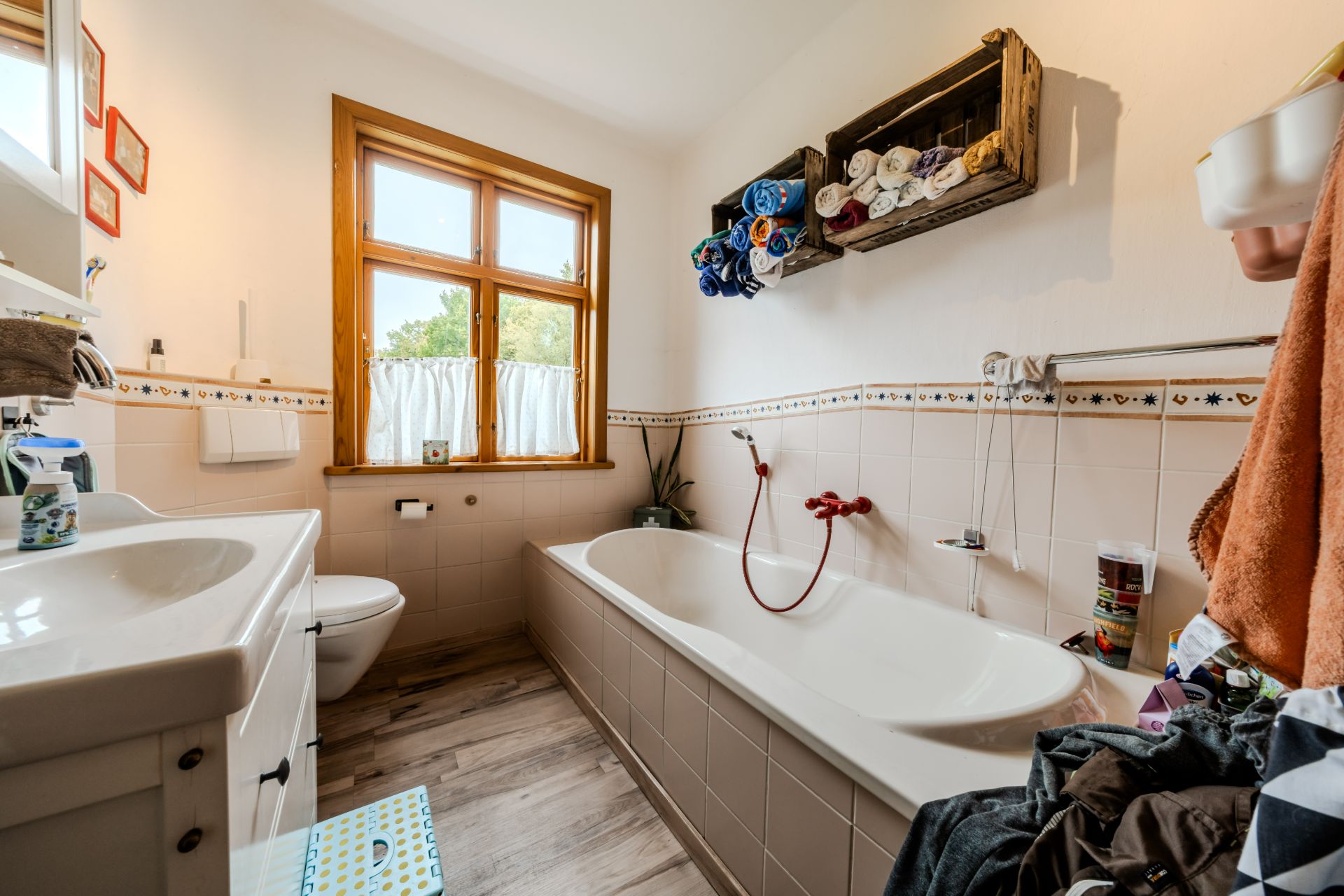 Helles Badezimmer mit Badewanne, Fenster, Waschbecken und Handtüchern an der Wand.
