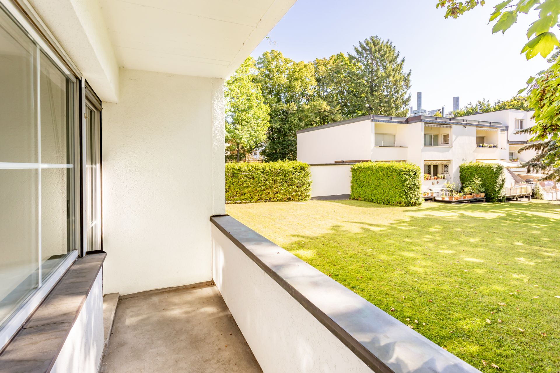 Blick von einer Terrasse auf einen grünen Garten und moderne Wohngebäude.