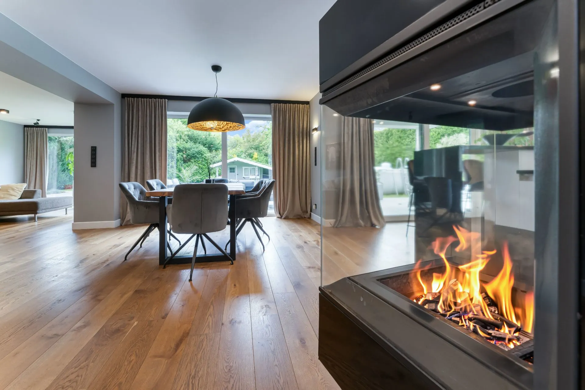 Modernes Wohnzimmer mit Kamin, Esstisch und großen Fenstern zum Garten.