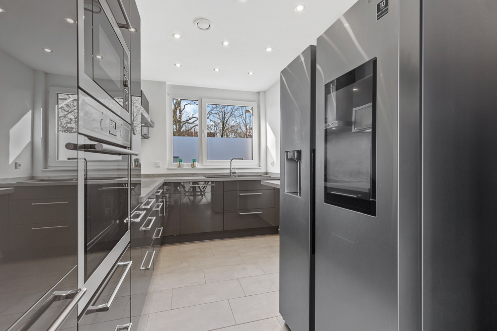 Moderne Küche mit glänzenden Schränken, großem Kühlschrank und drei Fenstern.