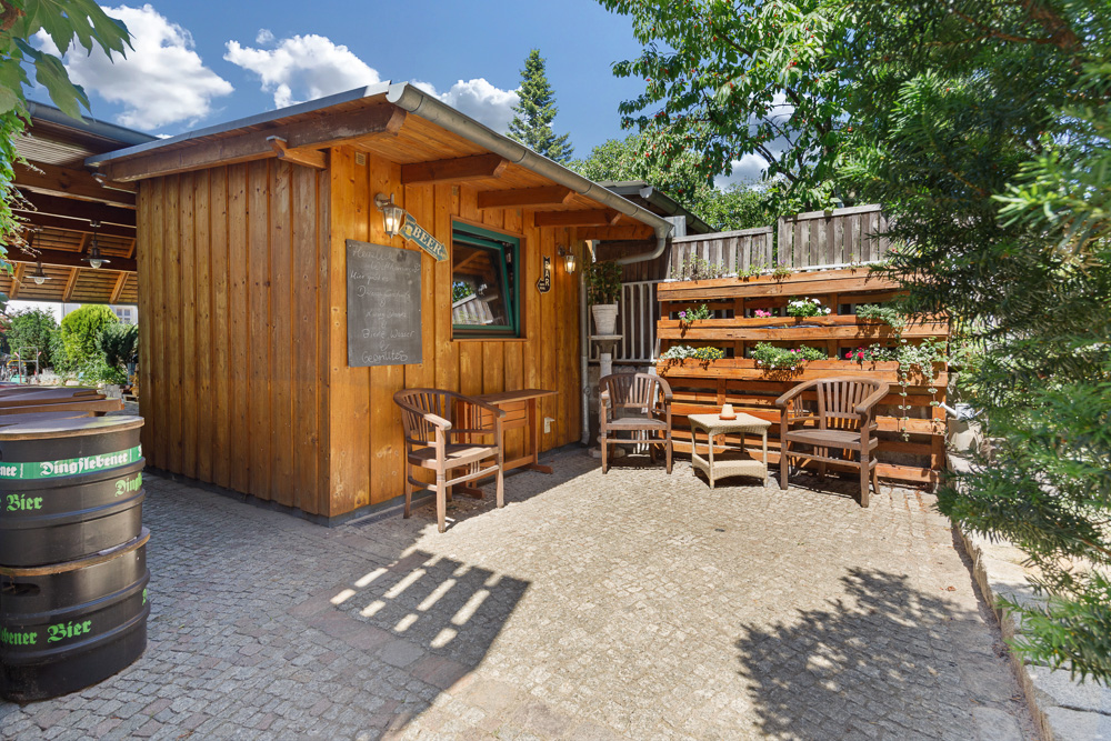 Gepflasterter Hof mit Holzhaus, Sitzbereich und vertikalem Blumenbeet aus Holzpaletten.