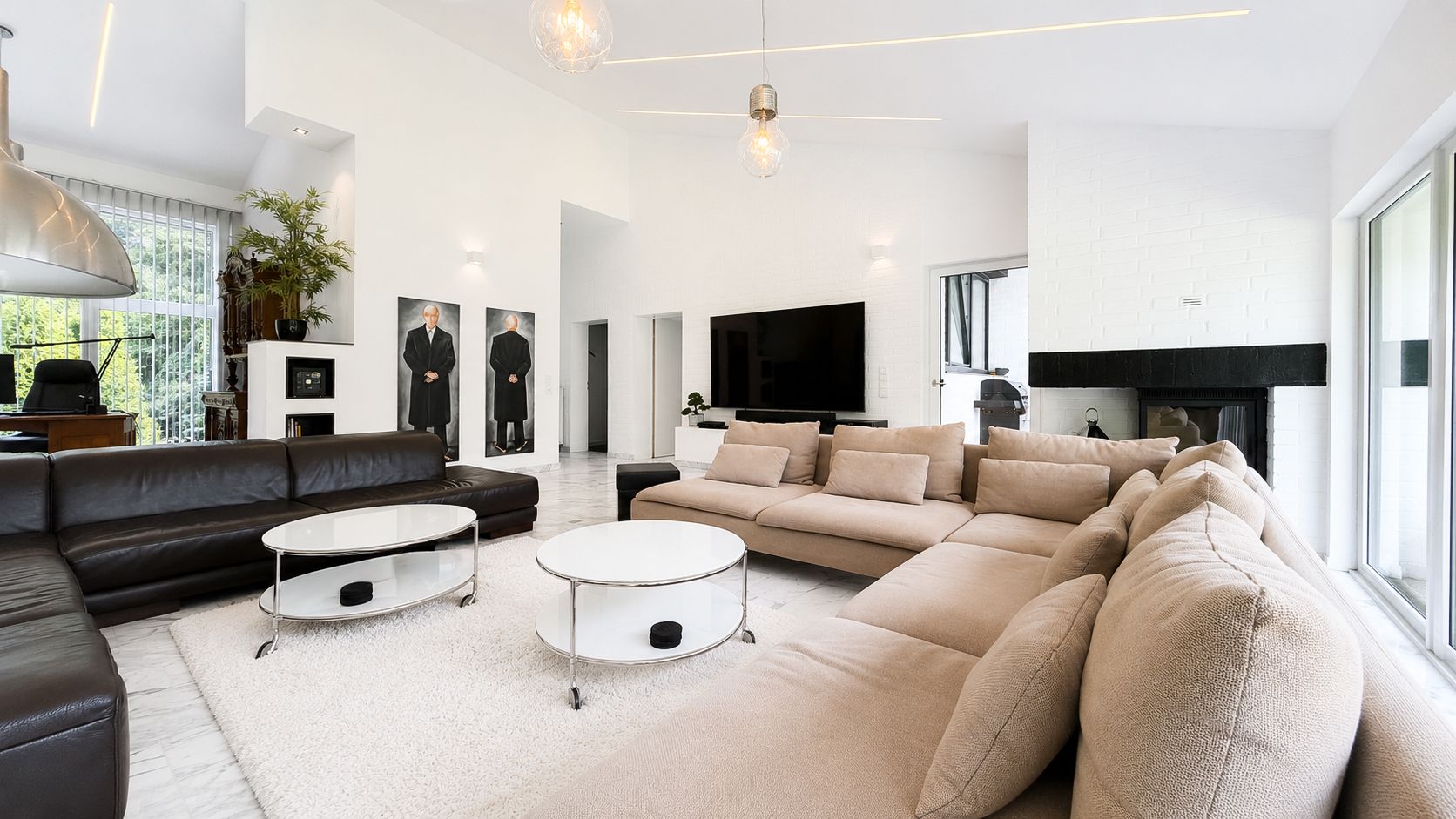 Modernes Wohnzimmer mit hellen Sofas, Couchtischen, Fernseher und großen Fenstern.