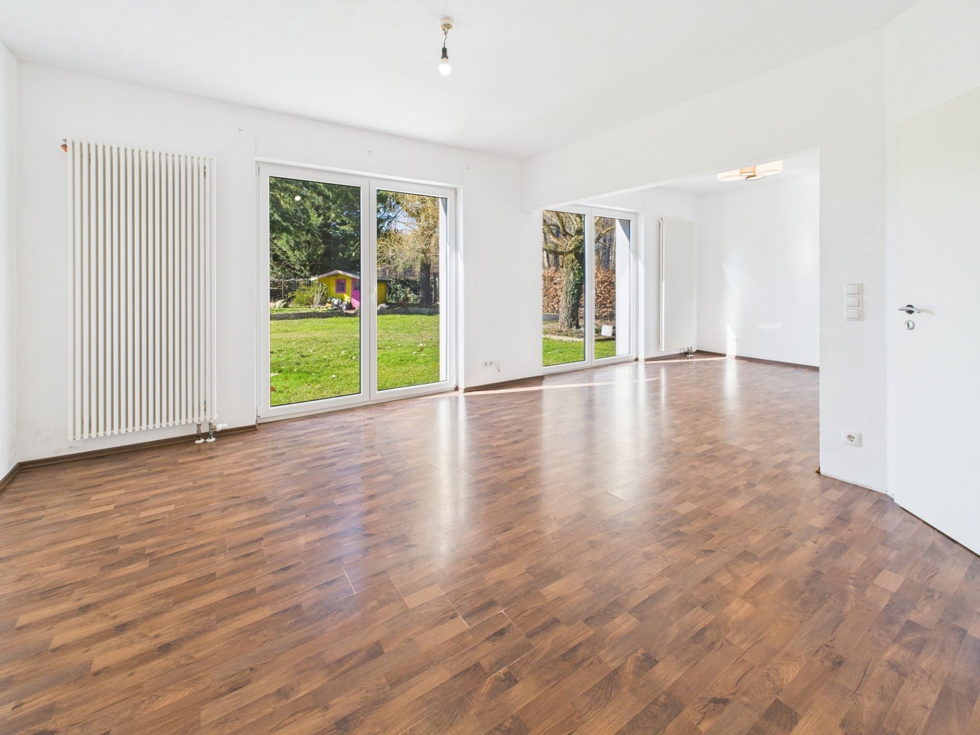 Helles, leeres Wohnzimmer mit Parkettboden und großen Fenstern zum Garten.