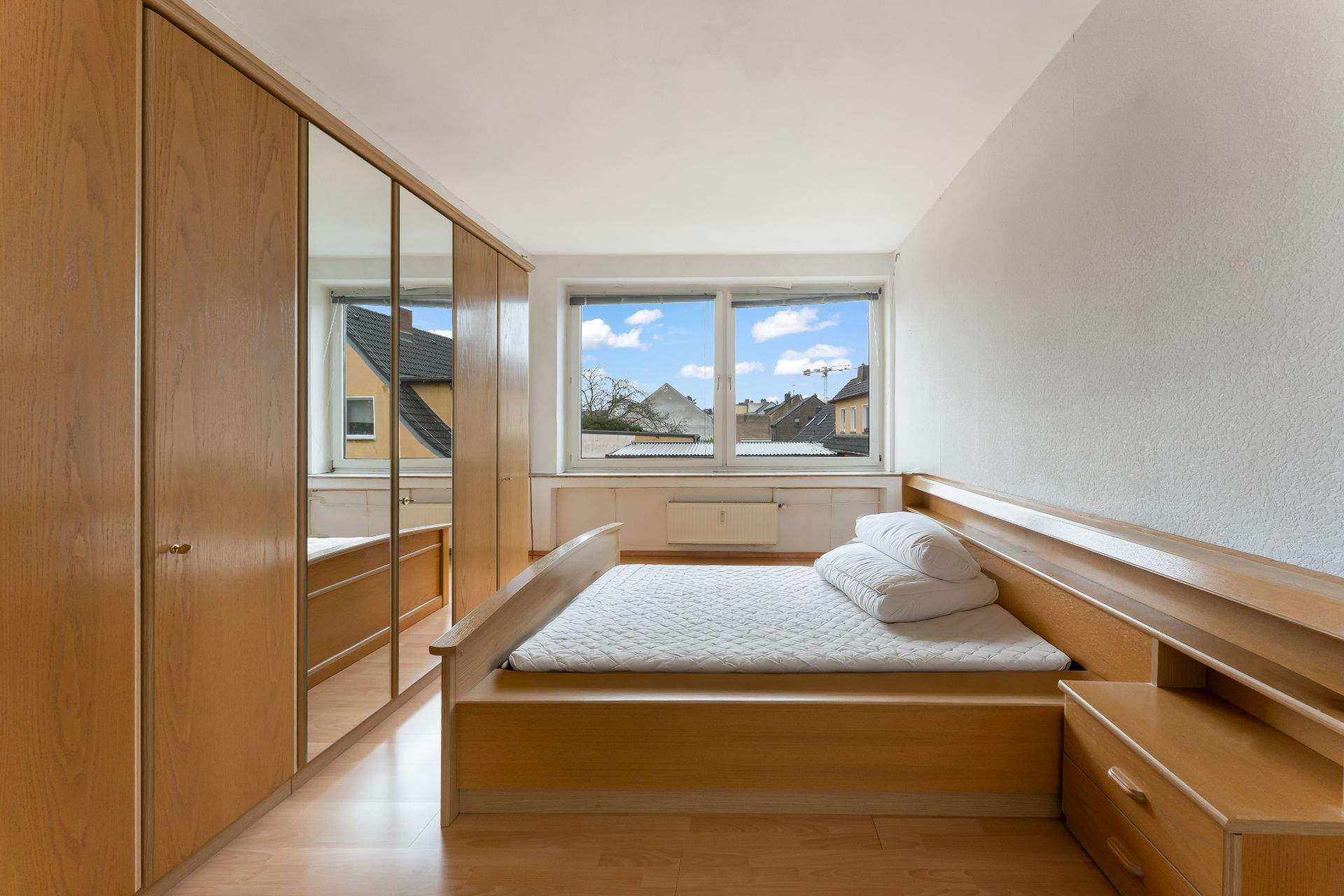 Schlafzimmer mit großem Fenster, Doppelbett und Holzschrank mit Spiegel.