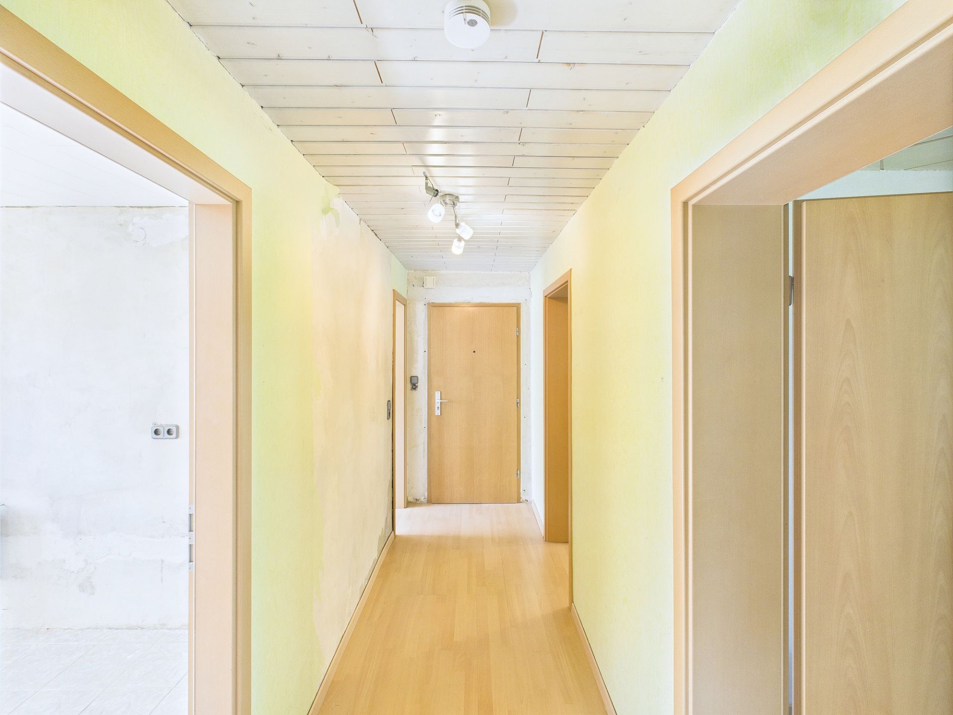 Heller Flur mit Holzboden, mehreren Türen und Deckenleuchte in einer Wohnung.