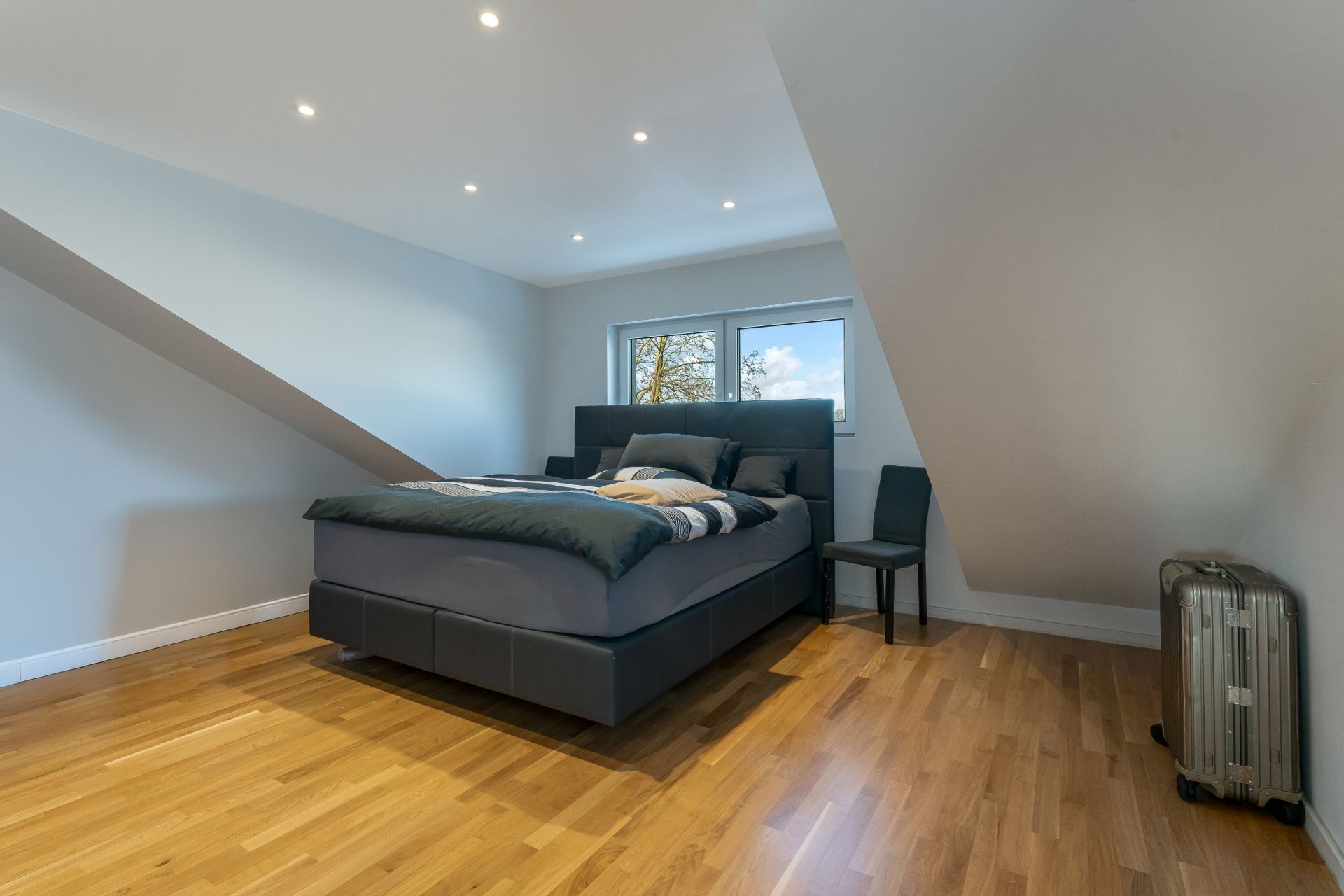 Modernes Schlafzimmer mit Doppelbett, zwei Stühlen und Parkettboden unter Dachschräge.