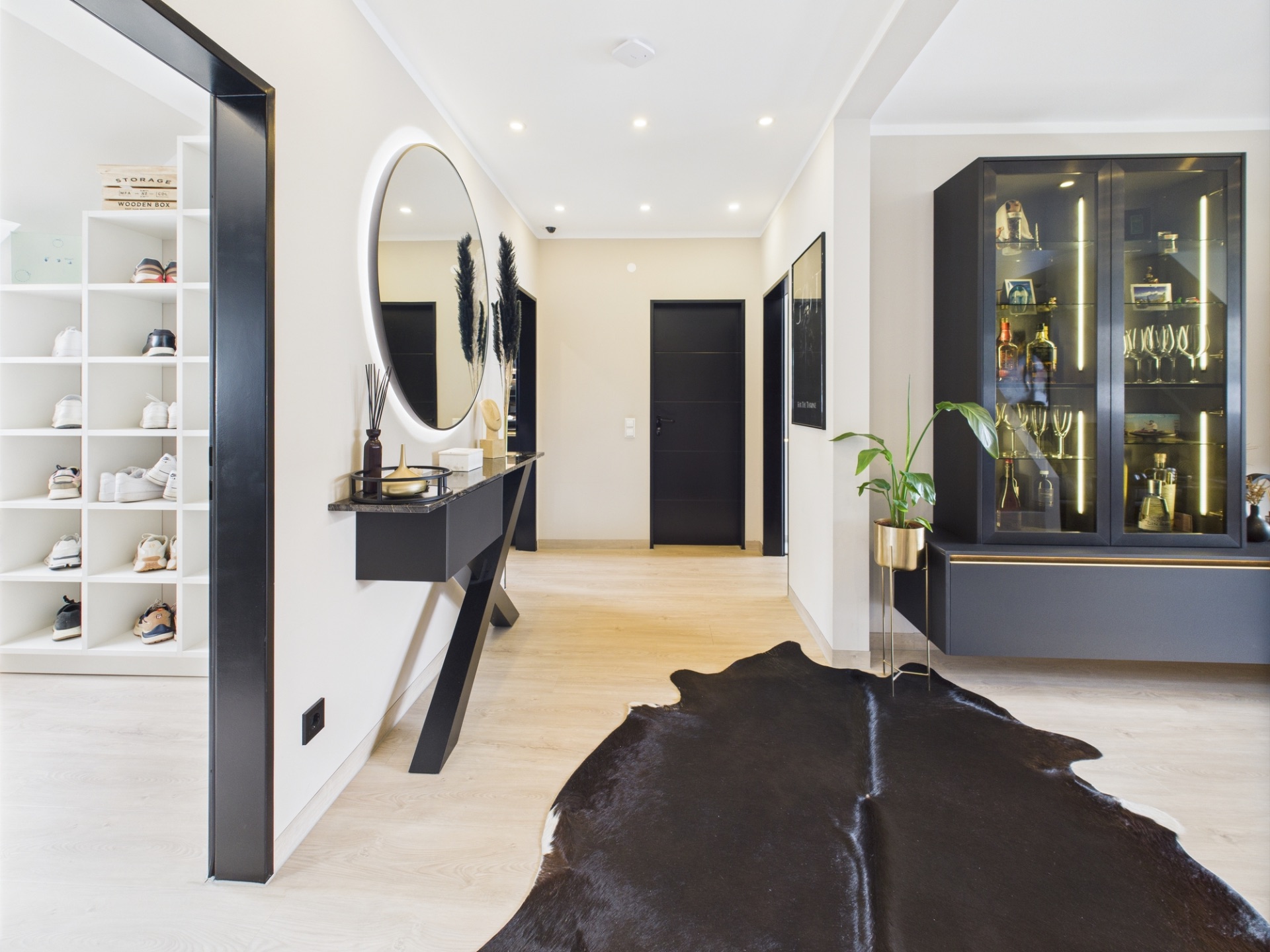 Moderner Flur mit rundem Spiegel, Schuhregal, Vitrine und schwarzem Teppich.