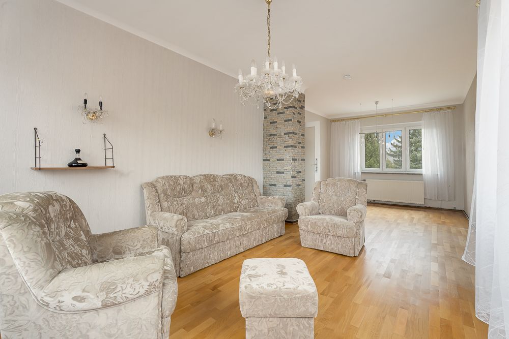Helles Wohnzimmer mit floral gemusterten Sofas, Sessel, Hocker, Kronleuchter und großem Fenster.