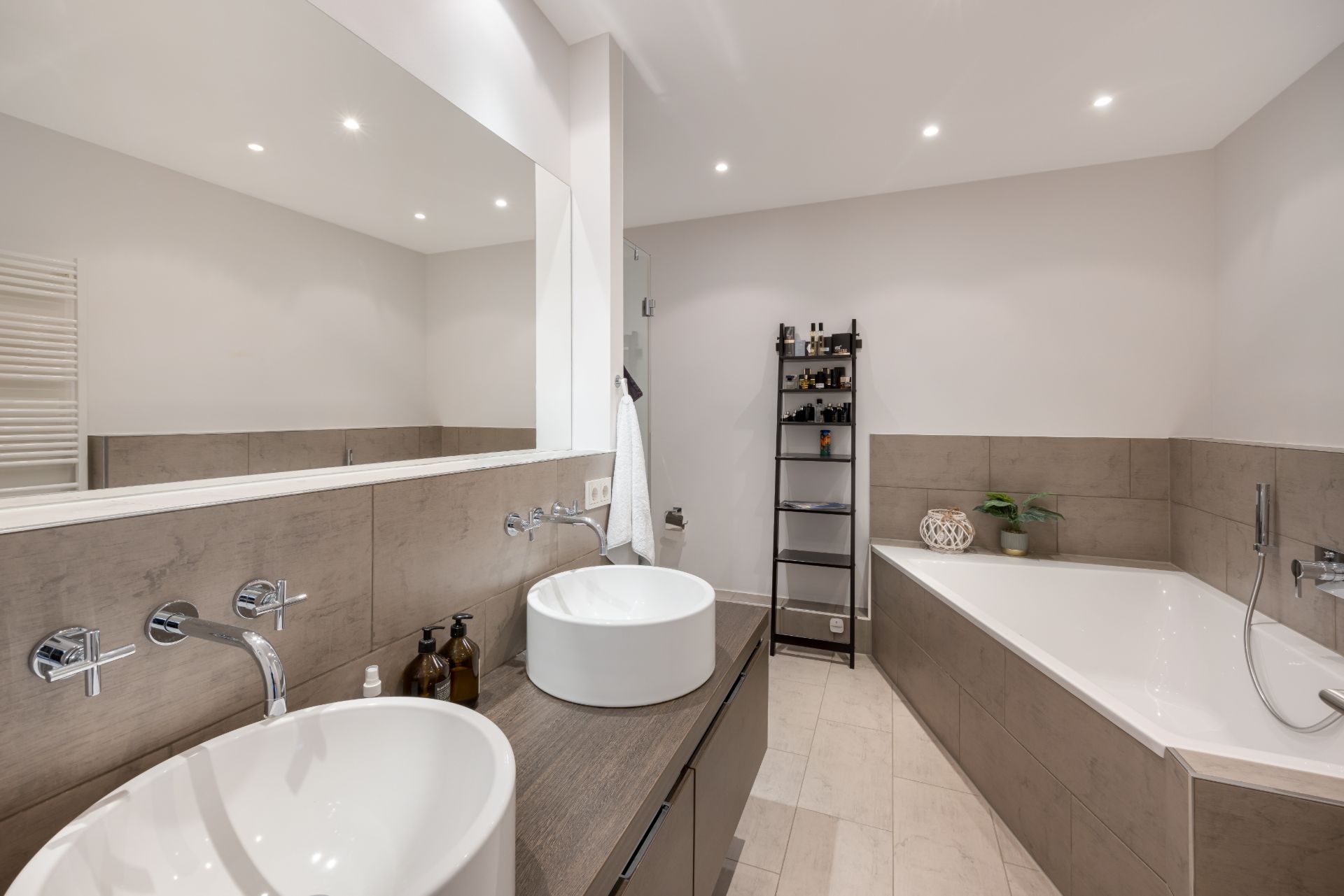 Modernes Badezimmer mit zwei Waschbecken, Eckbadewanne und Regal mit Pflegeprodukten.
