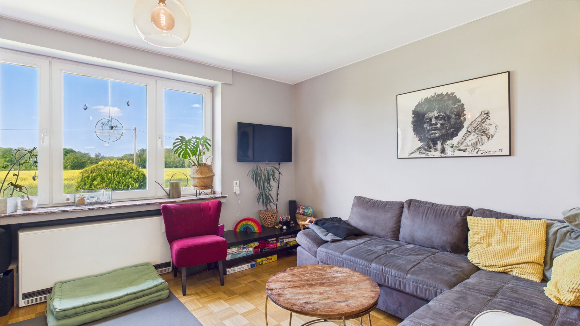 Helles Wohnzimmer mit großem Sofa, rundem Tisch, Sessel und dekorativem Bild an der Wand.
