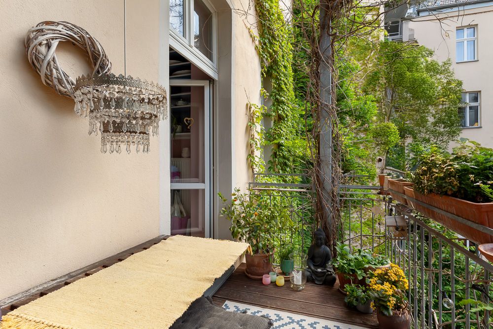 Kleiner Balkon mit Pflanzen, Teppich, Dekoration und Blick auf grüne Bäume.