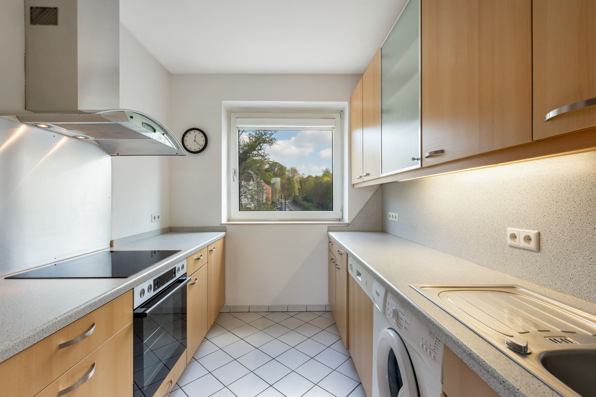 Helle, moderne Einbauküche mit Holzfronten, Elektroherd, Spüle, Waschmaschine und Fenster.