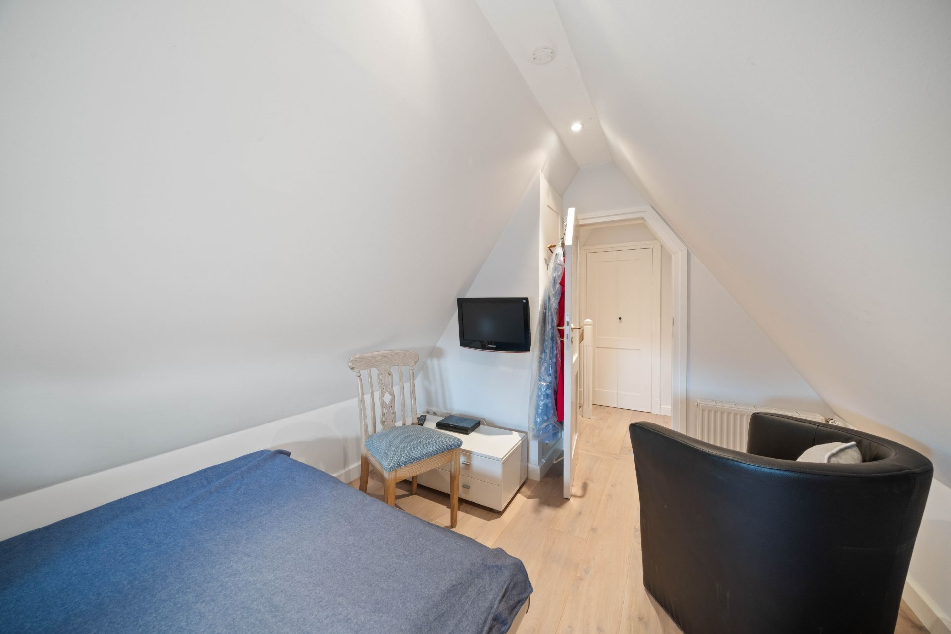 Kleines Dachzimmer mit Bett, Stuhl, Sessel, Fernseher und hellem Holzboden.