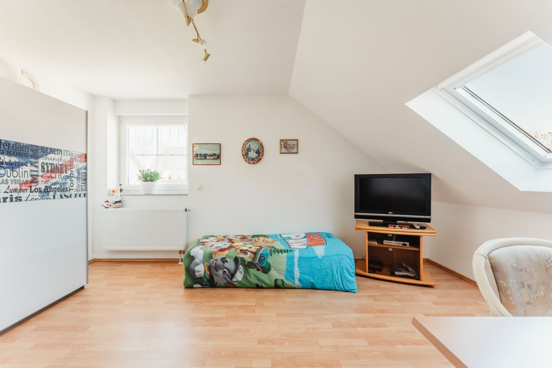 Helles Schlafzimmer mit Kinderbett, TV, Fenster und Dachschräge.