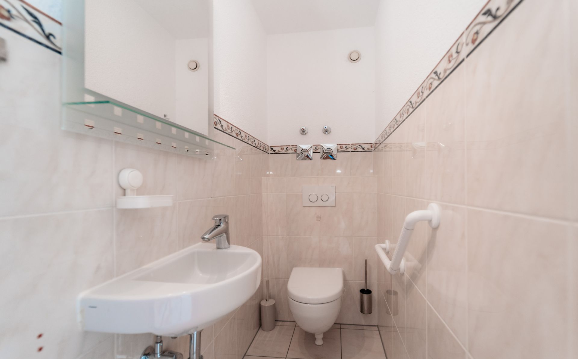Kleines Badezimmer mit Hängetoilette, Waschbecken und Haltegriff an der Wand.