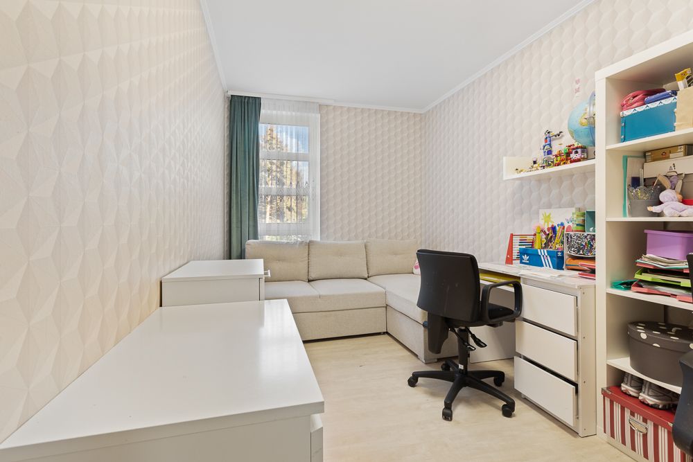 Helles Arbeitszimmer mit Schreibtisch, Regal, Sofa und Fenster mit grünen Vorhängen.