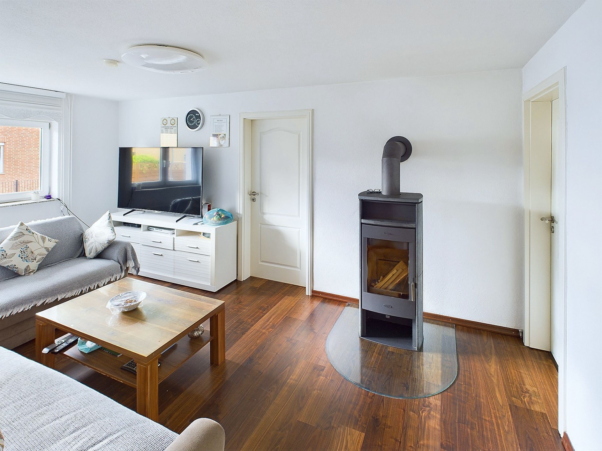 Helles Wohnzimmer mit Sofa, TV, Holztisch und Kamin auf dunklem Holzboden.