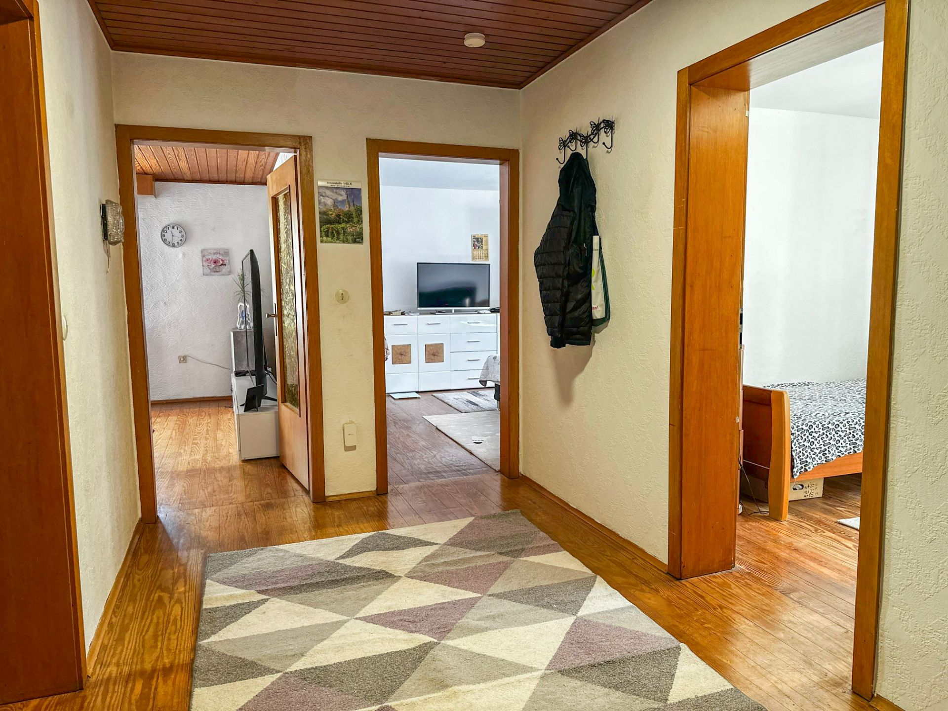 Flur mit Teppich und Holzboden, Türen führen zu einem Wohnzimmer und Schlafzimmer.