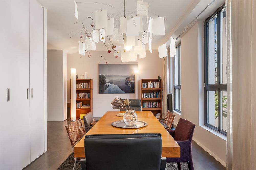 Esszimmer mit Holztisch, Stühlen, Bücherregalen und großem Fenster.