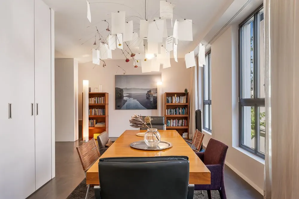 Esszimmer mit Holztisch, Stühlen, Bücherregalen und großem Fenster.