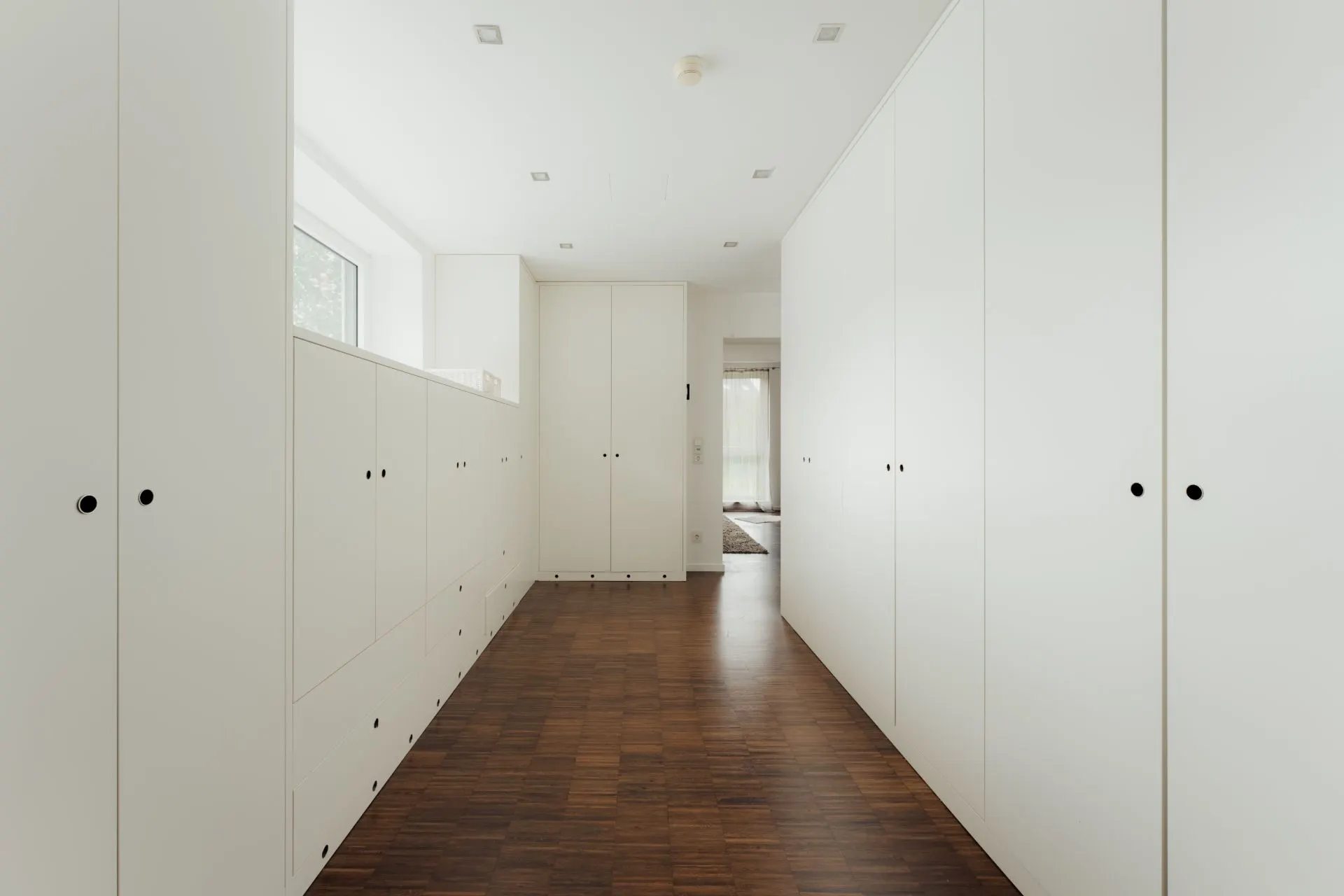Heller Flur mit weißen Einbauschränken und dunklem Holzboden.