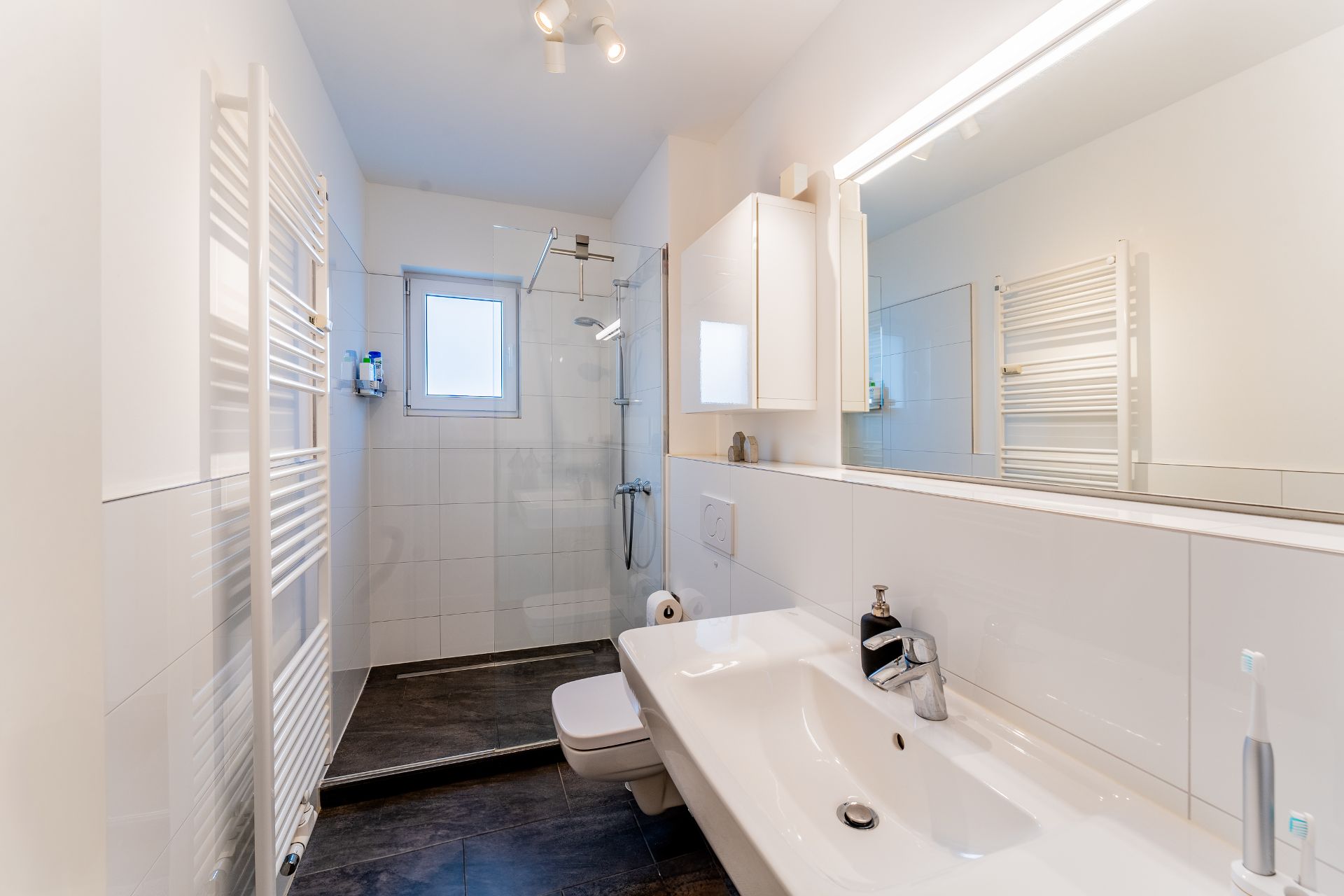 Modernes Badezimmer mit Dusche, großem Spiegel, Waschbecken und Handtuchheizkörper.