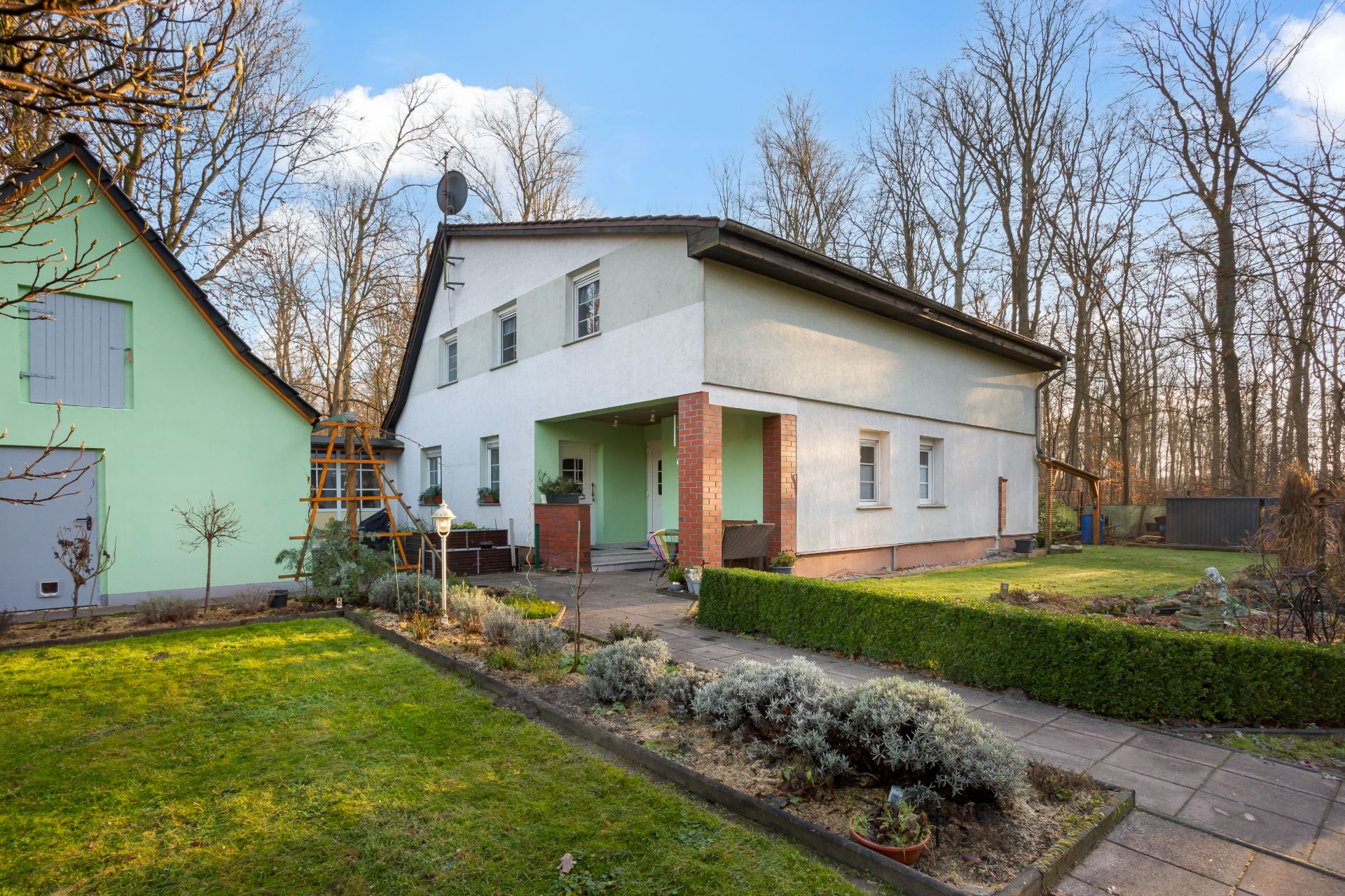 Zweistöckiges Wohnhaus mit Garten und kleinem Nebengebäude im Vordergrund.
