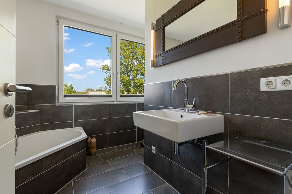 Modernes Badezimmer mit Badewanne, großem Fenster, Waschbecken und Spiegel.