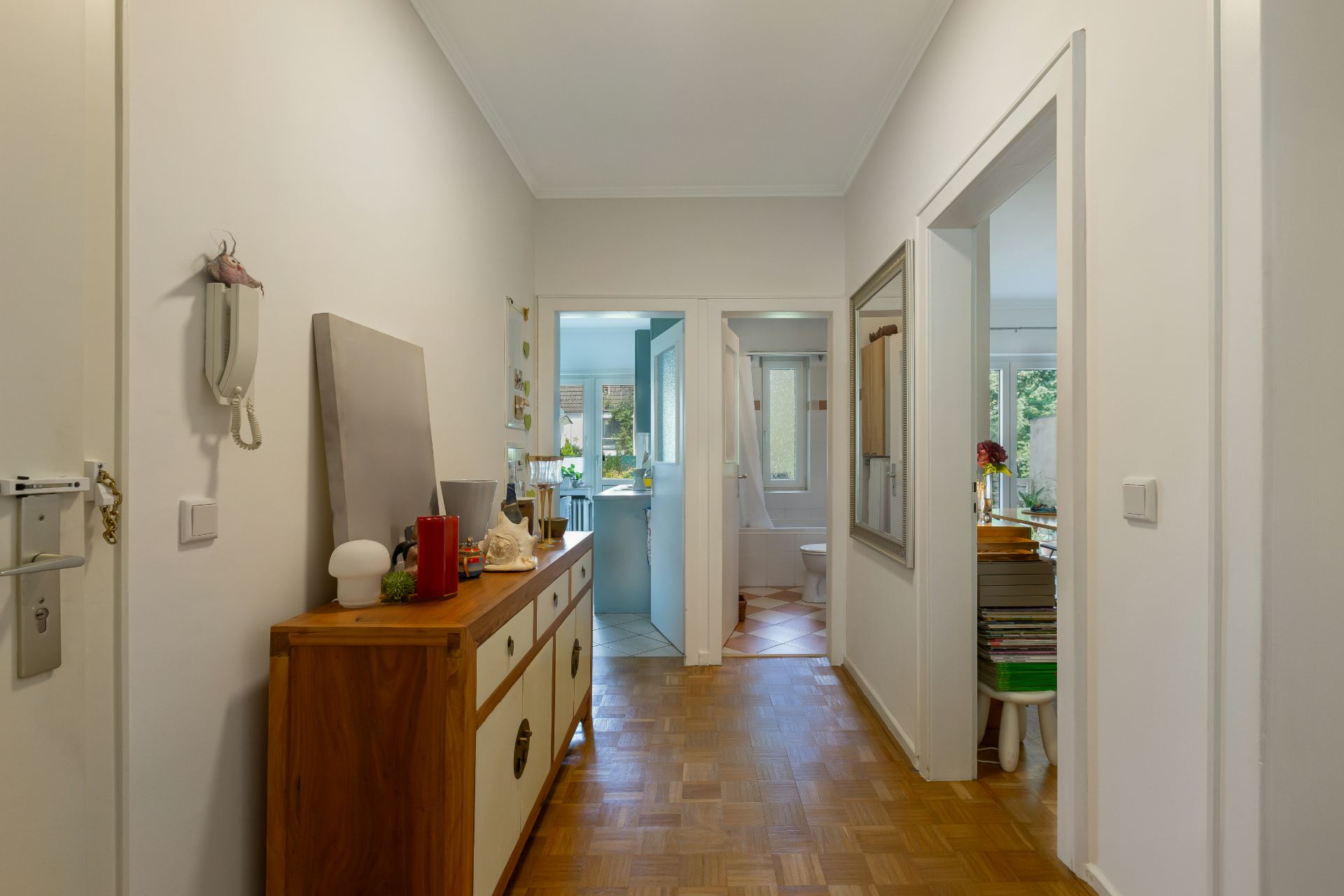 Heller Flur mit Holzboden, Kommode links und Blick in Bad, Küche und weiteres Zimmer.