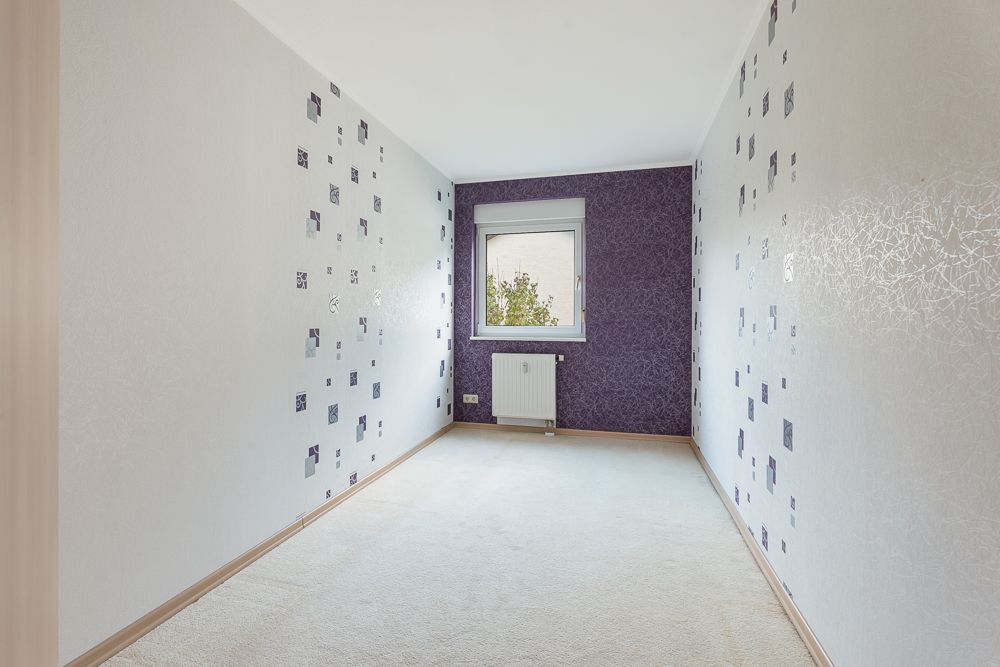 Schmaler, leerer Raum mit lila Akzentwand, Fenster und gemusterter Tapete.