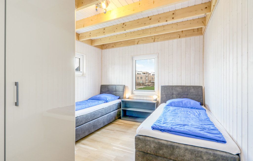 Zimmer mit zwei Einzelbetten, blauer Bettwäsche und Holzdecke, Fenster zeigt nach draußen.