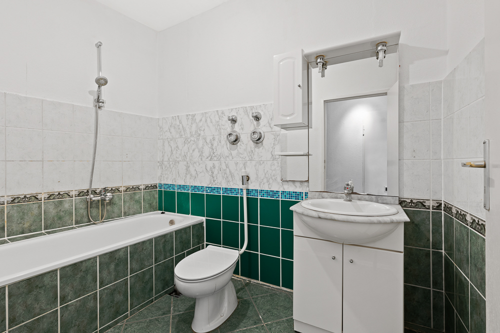 Badezimmer mit grünen Fliesen, Badewanne, Toilette und Waschbecken mit Spiegel.