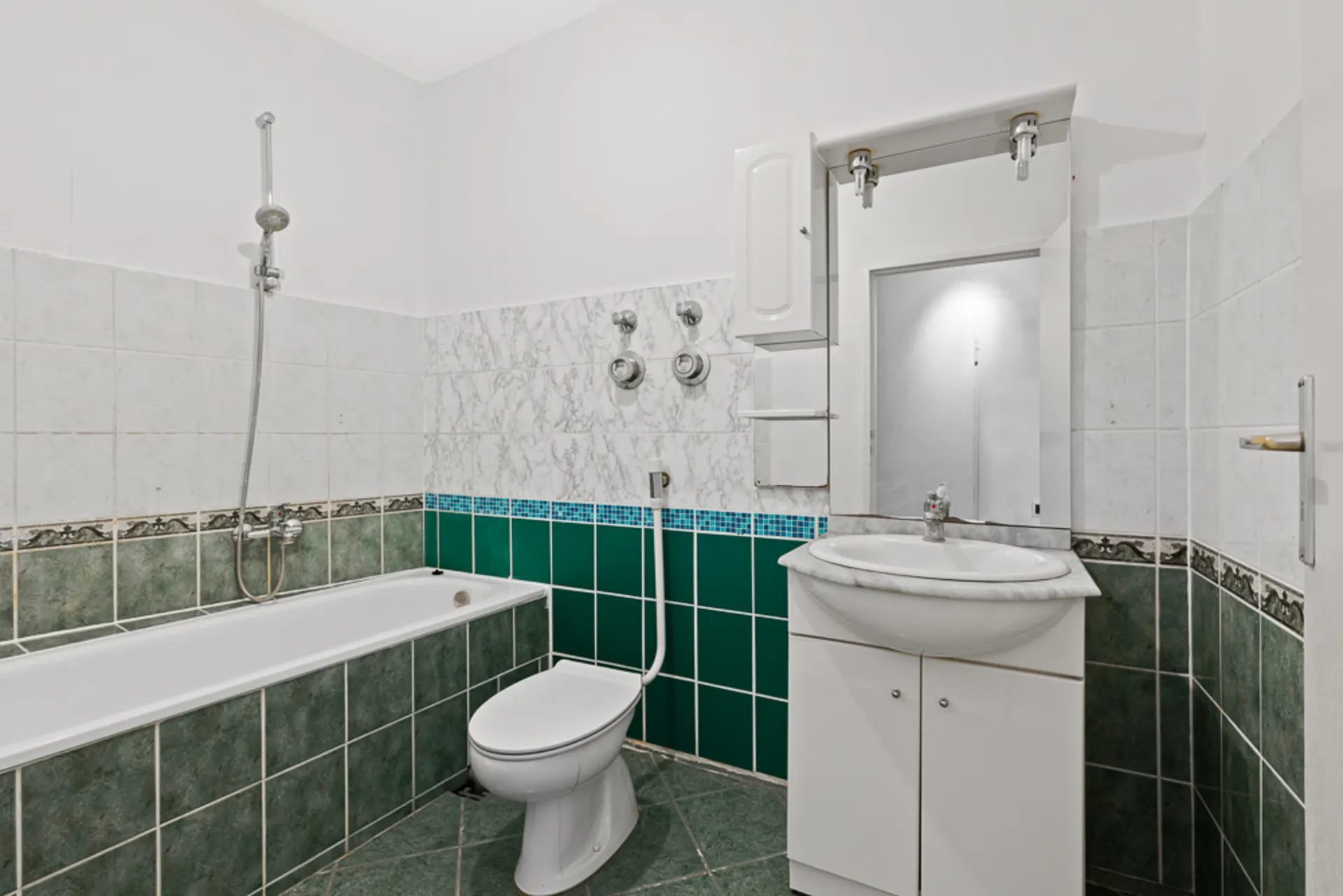 Badezimmer mit grünen Fliesen, Badewanne, Toilette und Waschbecken mit Spiegel.
