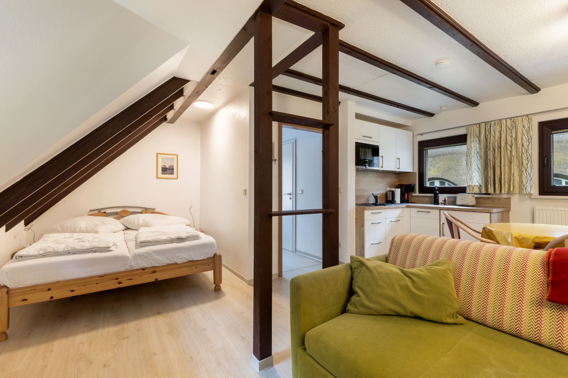 Wohnbereich mit Sofa, Doppelbett unter Dachschräge und offener Küche mit Essbereich.