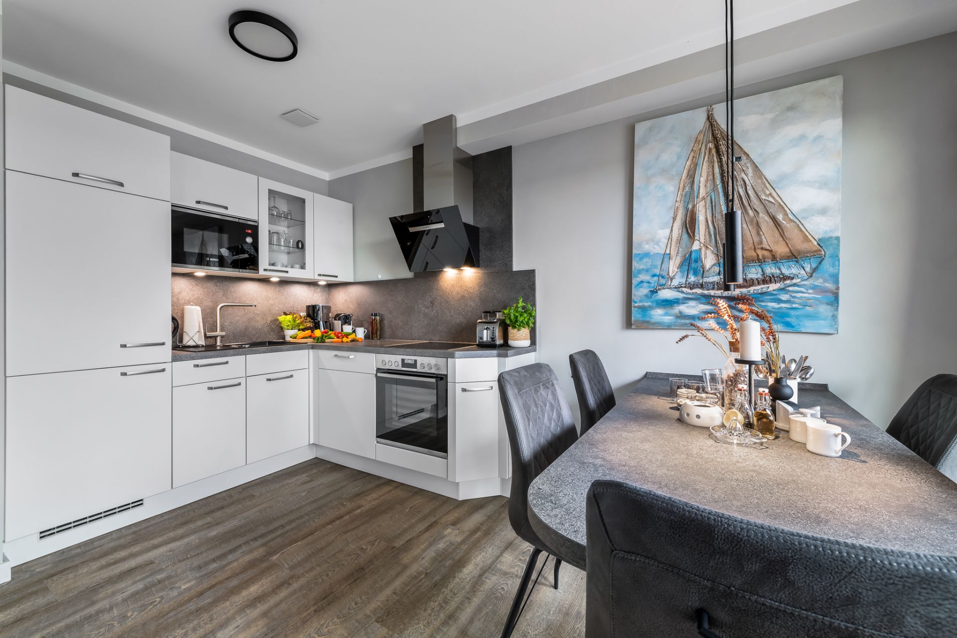 Moderne weiße Küche mit Esstisch und großem Gemälde eines Segelboots an der Wand.