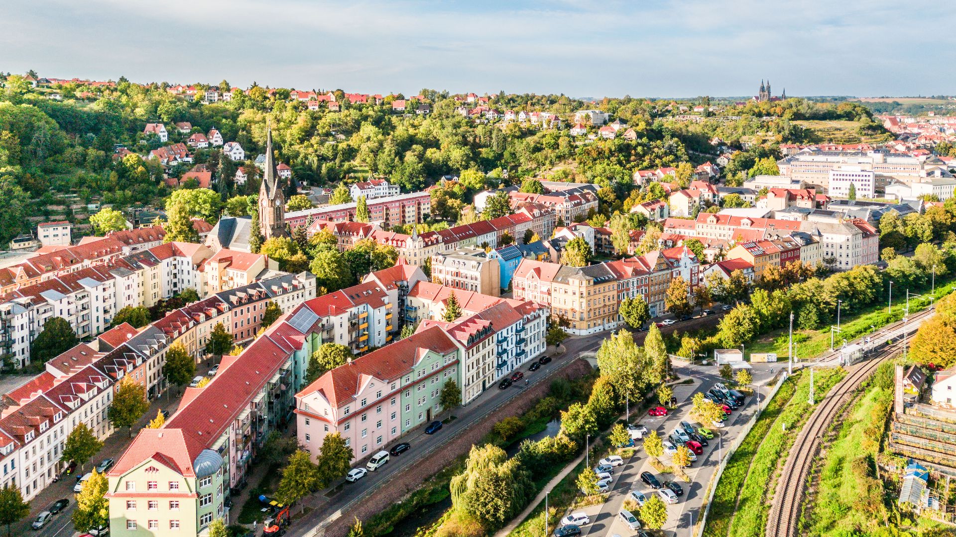 Luftaufnahme eines Wohngebiets mit bunten Häusern, Bäumen und parkenden Autos.