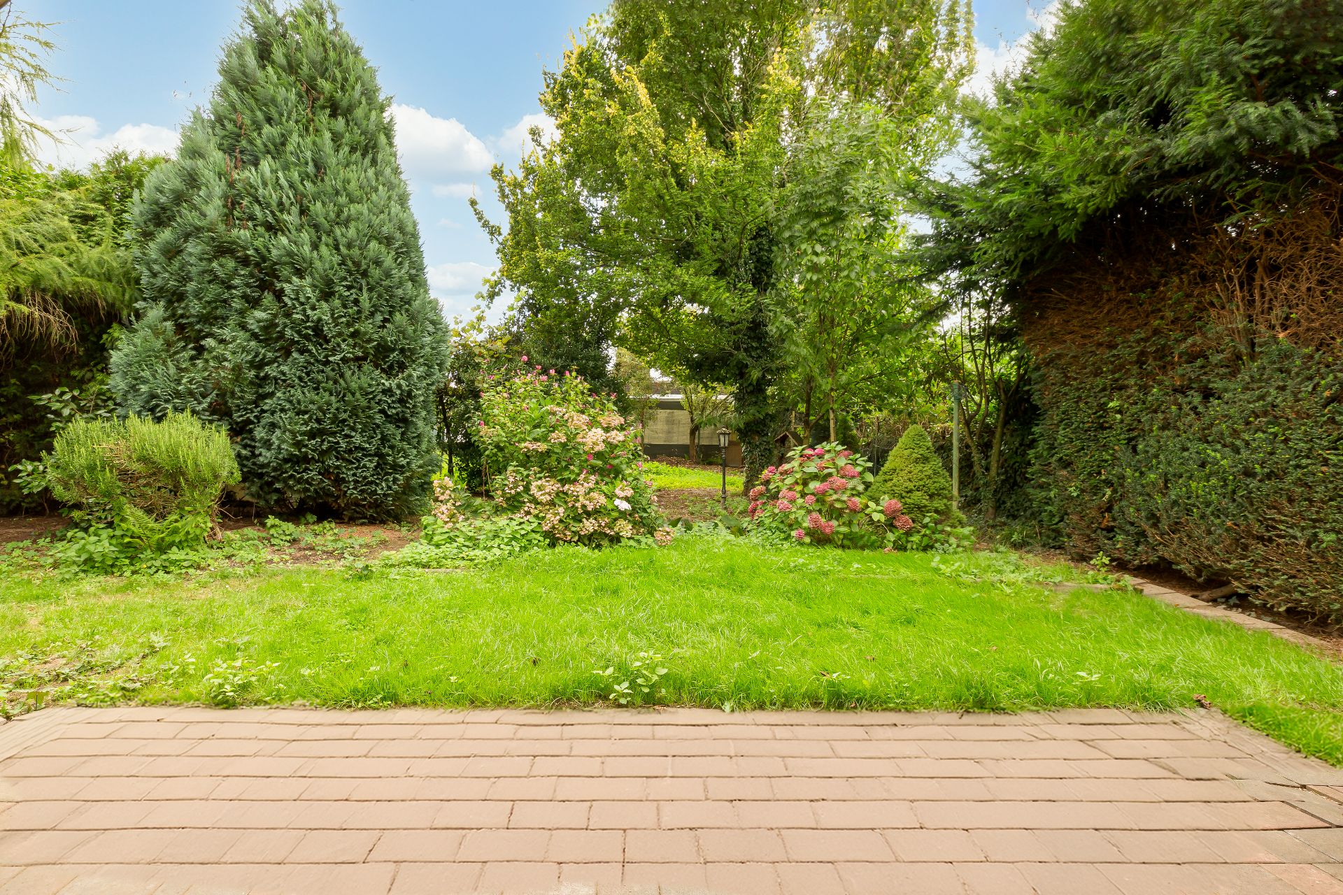 Blick auf einen grünen Garten mit Bäumen, Sträuchern und Rasen von einer Terrasse aus.