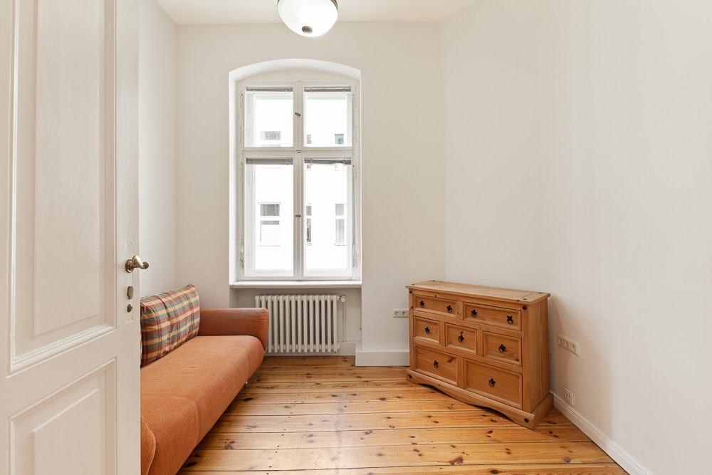 Heller Raum mit Holzboden, einem orangefarbenen Sofa und einer Holztokommode vor einem Fenster.