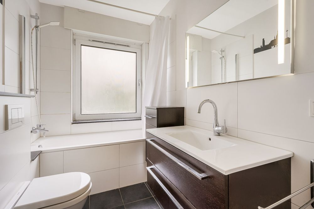 Modernes Badezimmer mit Badewanne, großem Spiegel und Waschbecken unter einem Fenster.