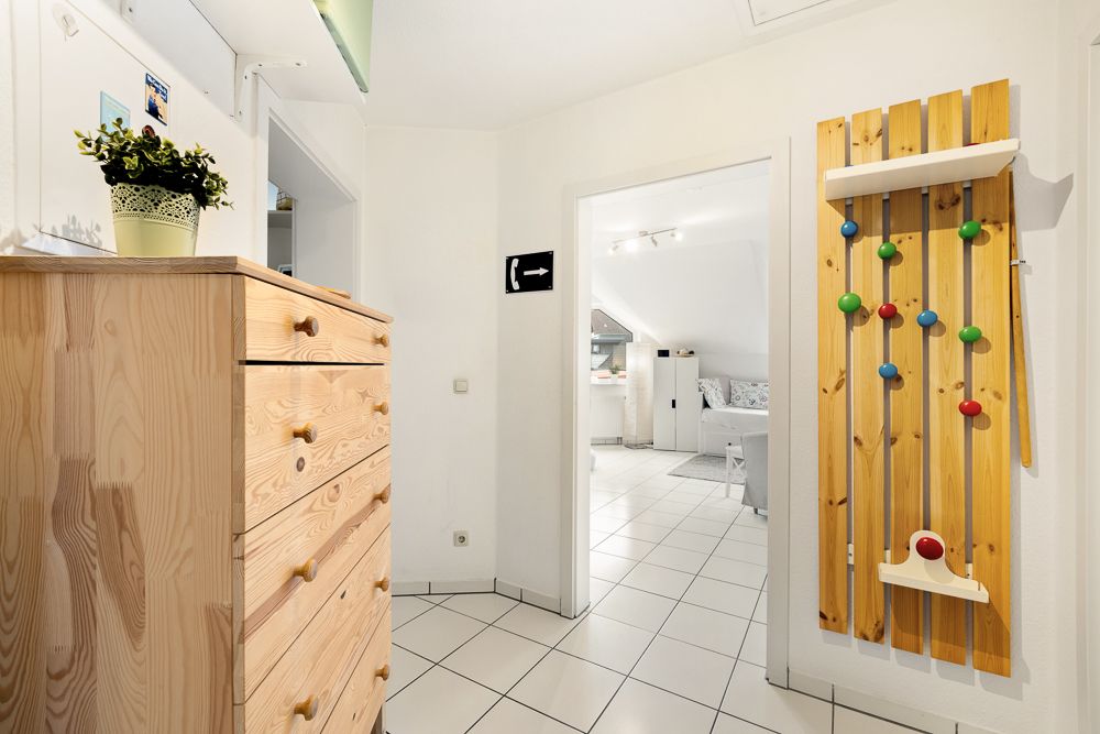 Flur mit Holzkasten, Pflanze darauf und buntem Holzspiel an der Wand, Blick ins Wohnzimmer.