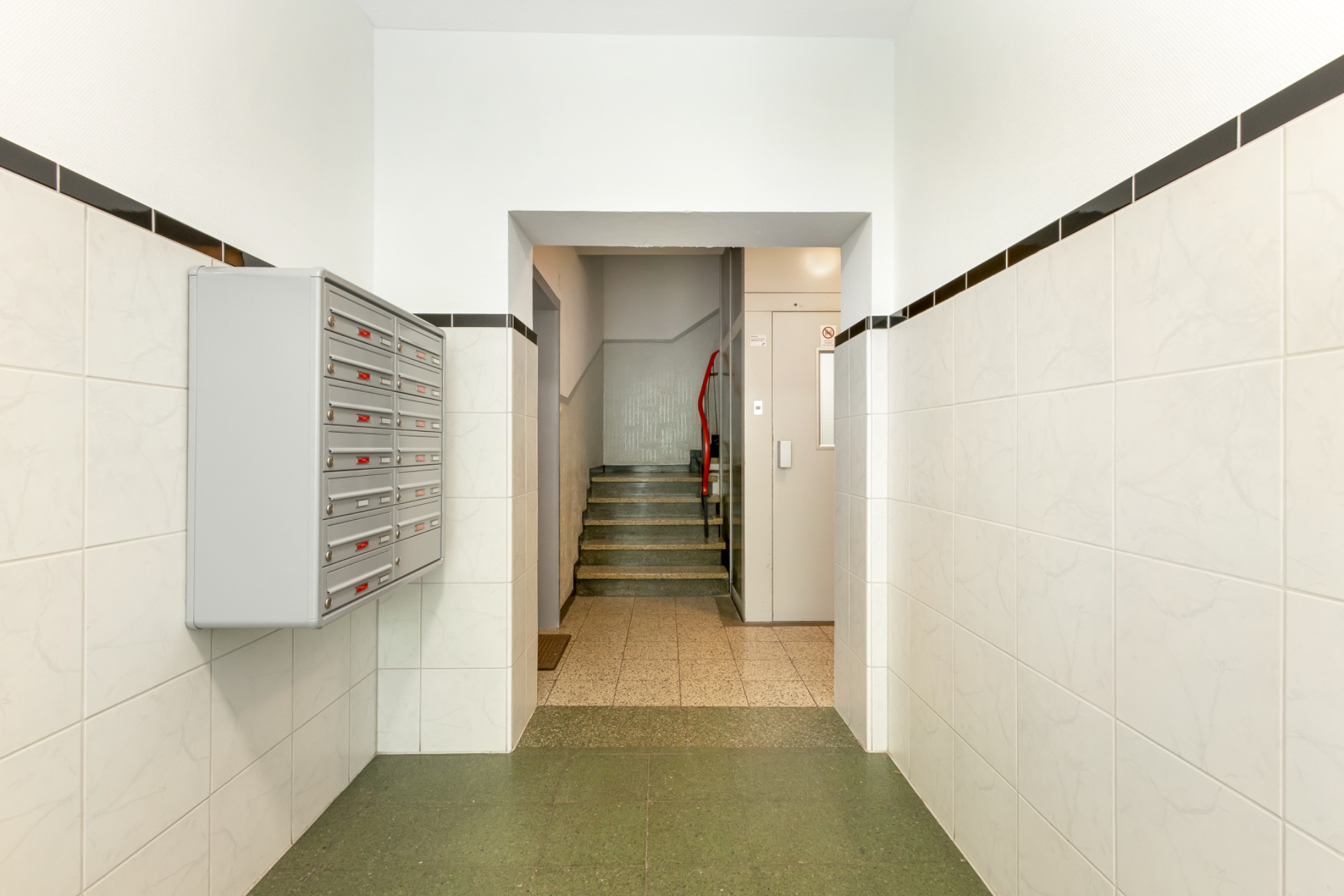 Eingangsflur mit Briefkästen an der Wand und Treppenaufgang im Hintergrund.