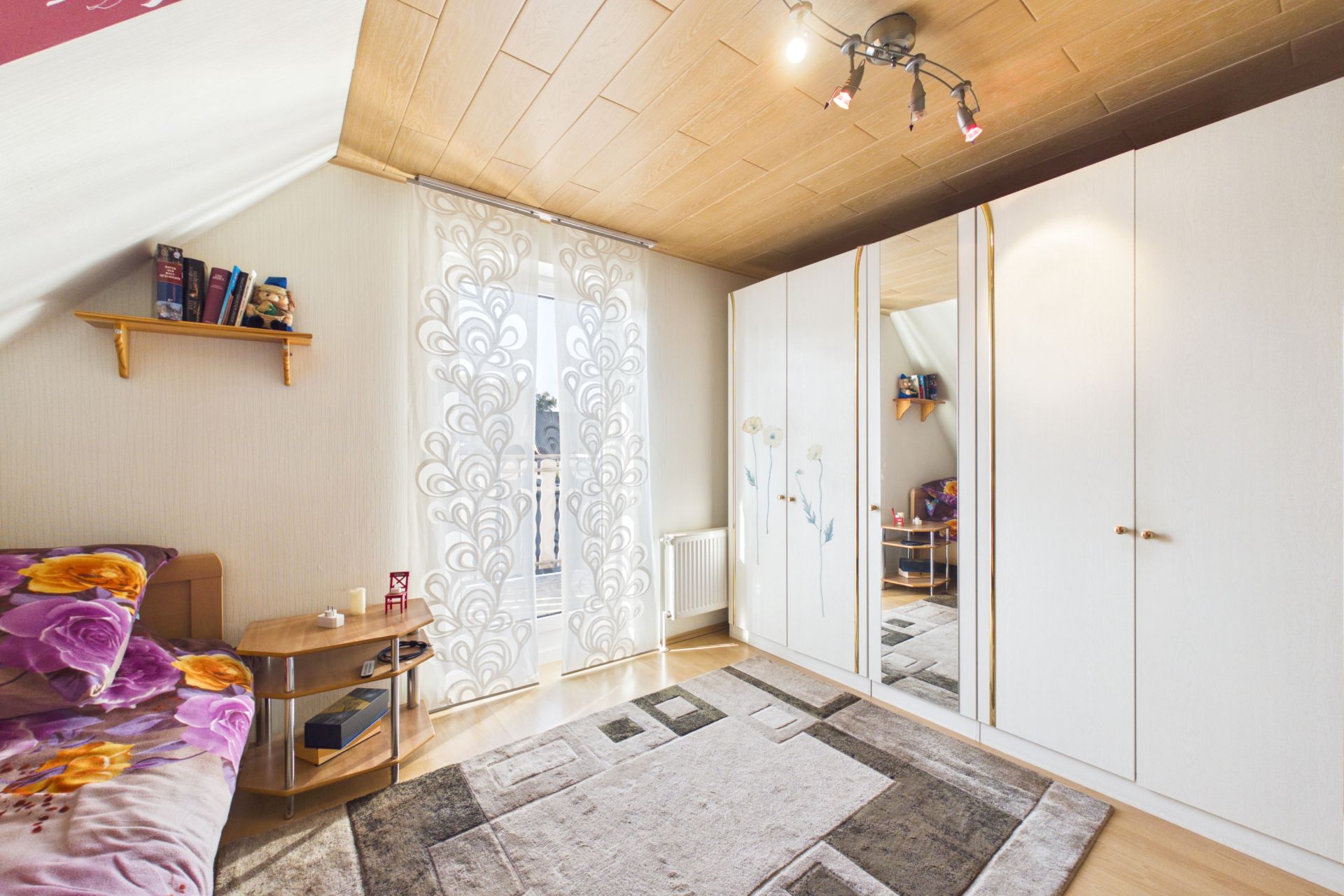 Helles Schlafzimmer mit großem Teppich, Kleiderschrank, Bett und Fenster mit Vorhang.