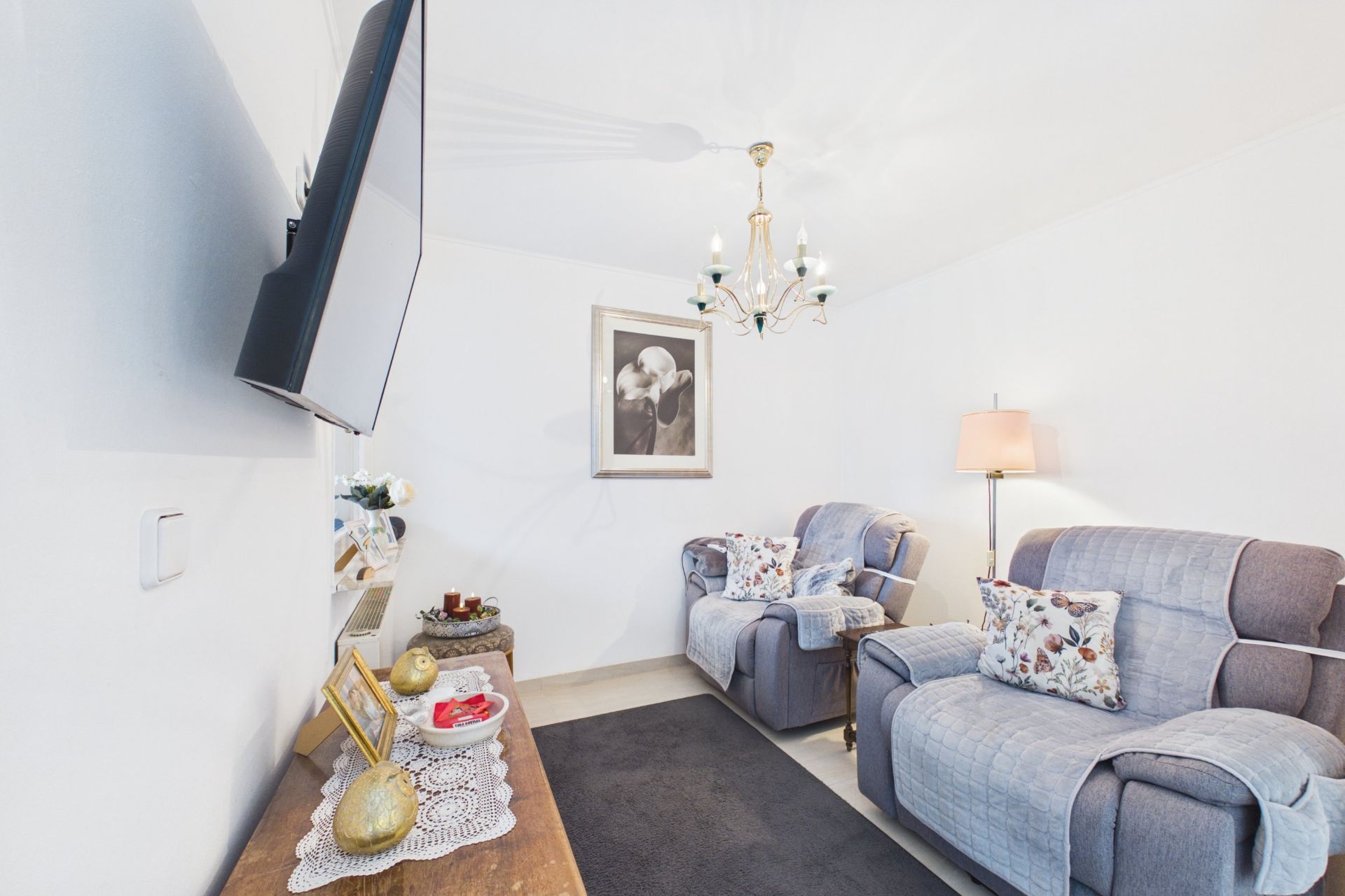 Wohnzimmer mit zwei grauen Sesseln, Wandbild, TV, Stehlampe und Beistelltisch.