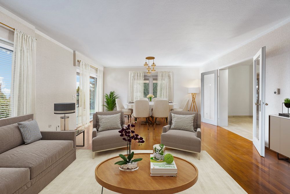 Helles Wohnzimmer mit Sofa, zwei Sesseln, Couchtisch und Essbereich mit sechs Stühlen.