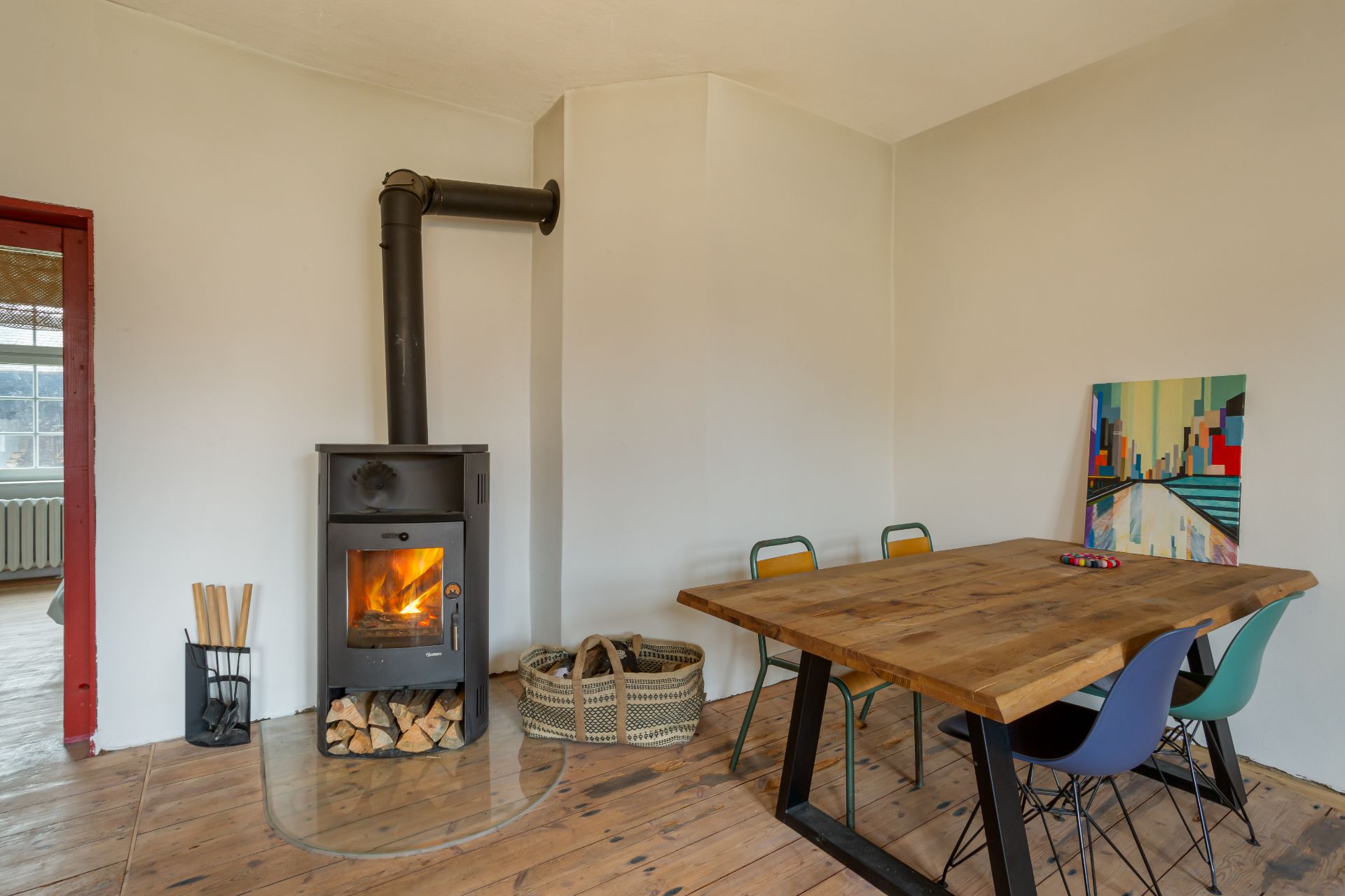 Essbereich mit Holzofen, Holztisch, bunten Stühlen und Holz auf Holzboden.