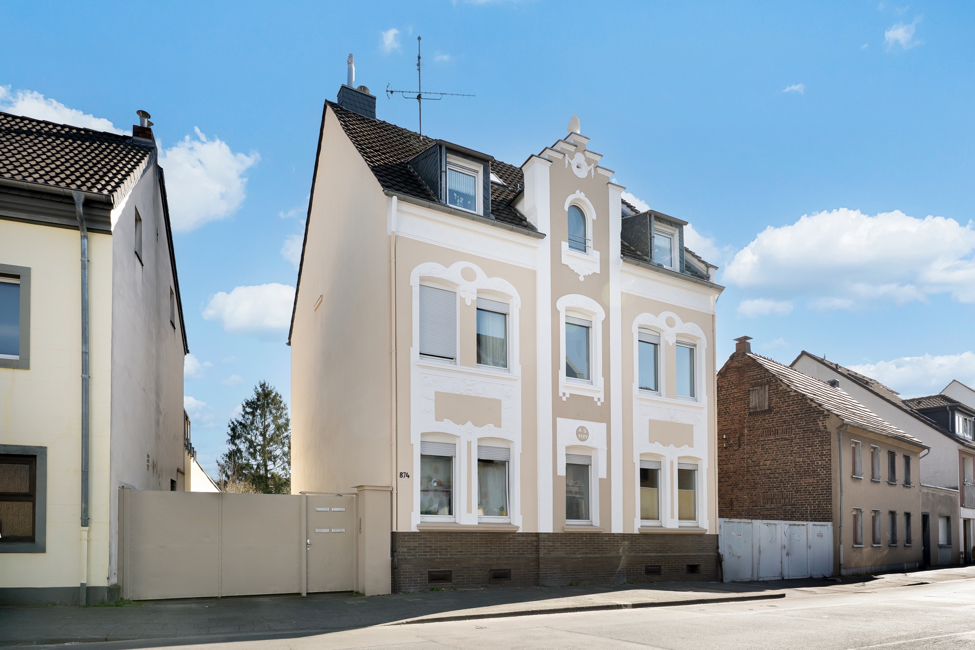 Dreistöckiges Wohnhaus mit weißer Fassade und steilem Dach an einer ruhigen Straße.