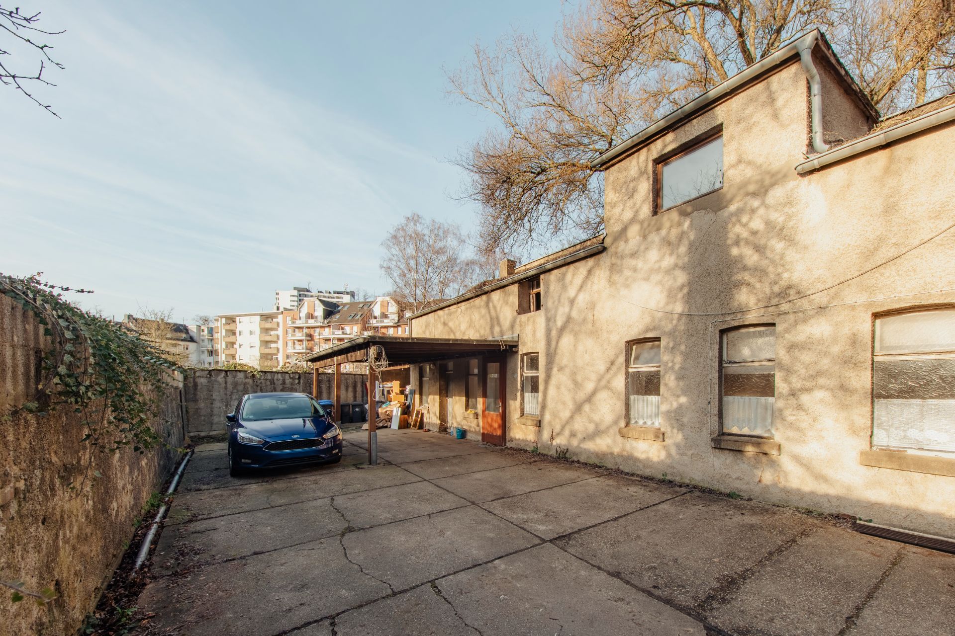 Hof eines Wohnhauses mit geparktem Auto, betonierter Fläche und altem Gebäude.