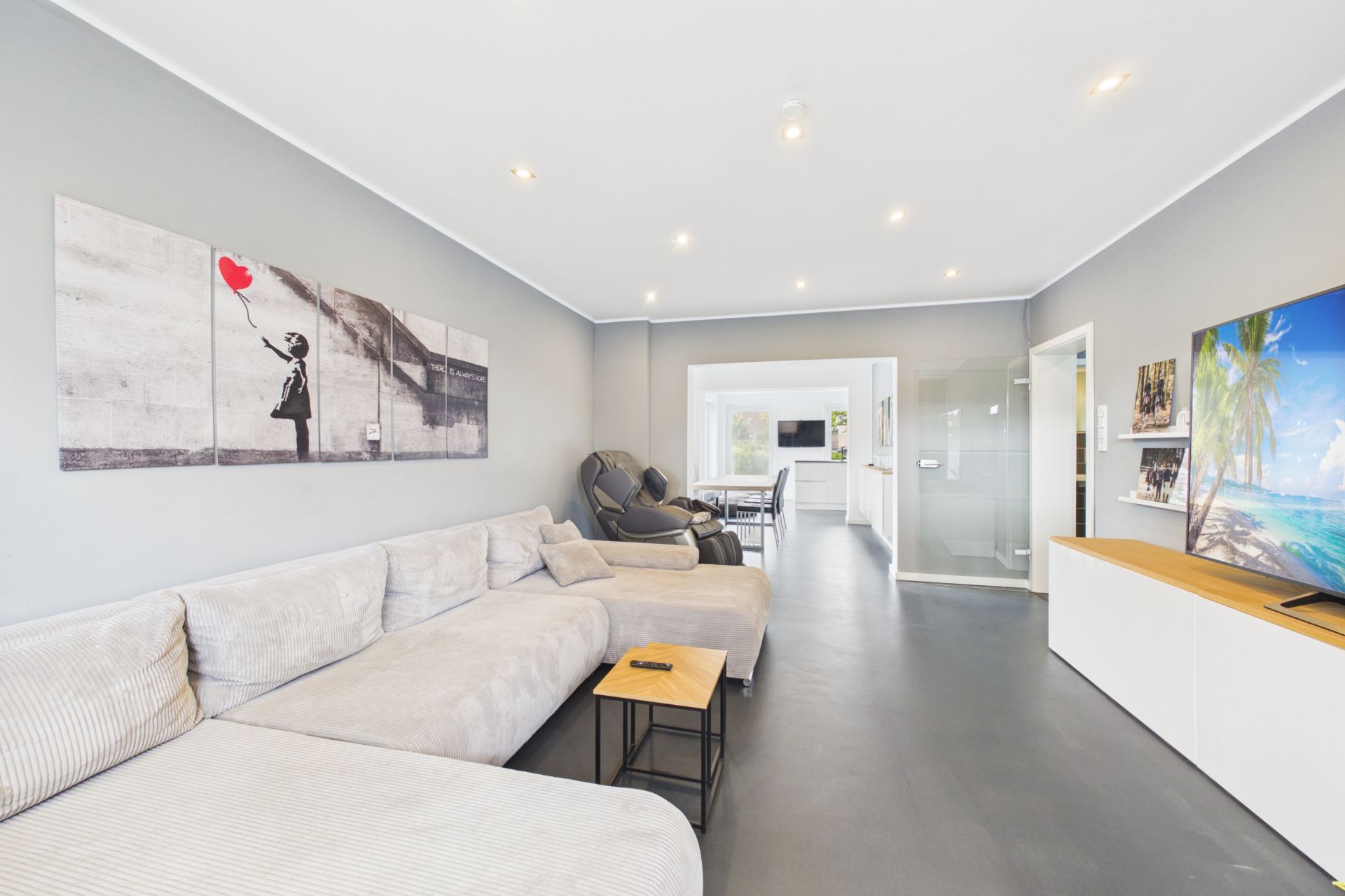 Modernes Wohnzimmer mit großem Sofa, Wandbild, Fernseher und Blick in Essbereich.