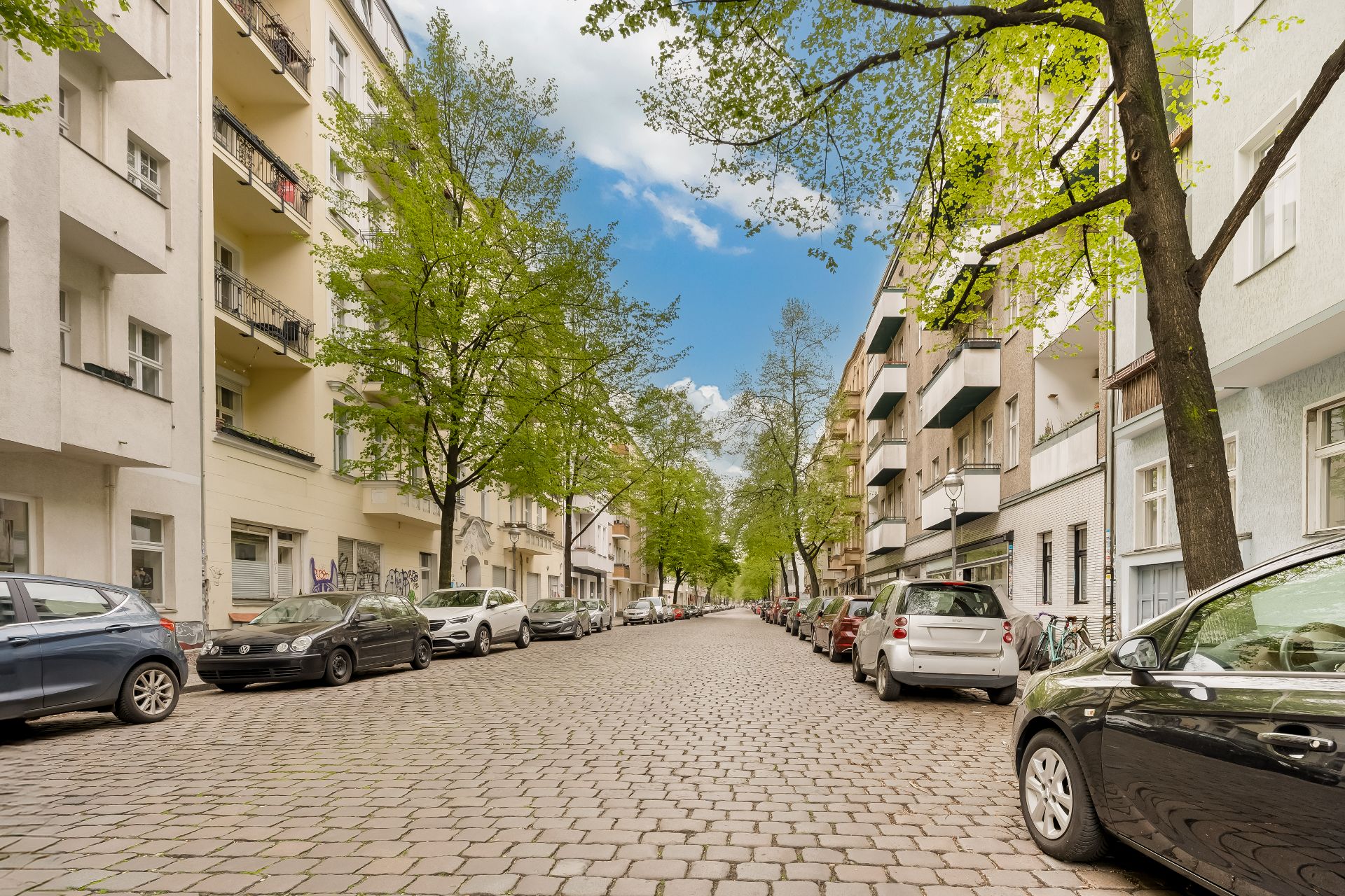 Baumgesäumte Wohnstraße mit geparkten Autos und mehrstöckigen Wohngebäuden.